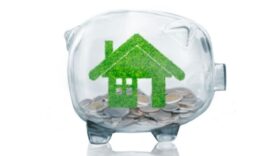 home savings concept with grass growing in shape of house inside transparent piggy bank