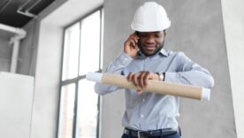 Construction worker looking at his watch and holding construction drawings