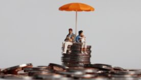 Pile of coins with a toy family sitting on top of the pile with a toy umbrella over them