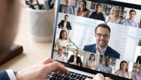 A business man in a suit on the computer with people all attending the call on the screen