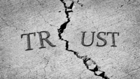 Concrete ground with a crack going through the center. The word TRUST is split up between the crack