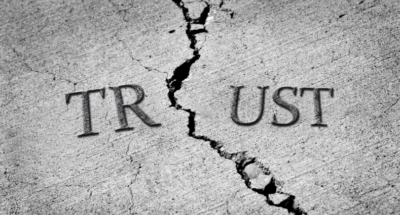 Concrete ground with a crack going through the center. The word TRUST is split up between the crack