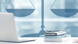 Legal scales in the background and a laptop on a desk with notepads and a pen surrounding it