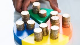 Plastic pie chart with coins on each where One piece is being taken out of the group by a hand