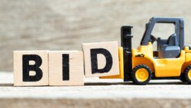 Toy tow truck picking up wooden bricks with the word BID painted on them