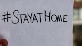 A man's hand holding a piece of paper with "stayathome" handwritten on it