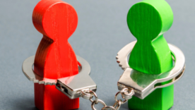 Two wooden playing piece people are handcuffed to each other