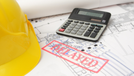 "Delayed" stamp on a drawing with hard hat and calculator in the background