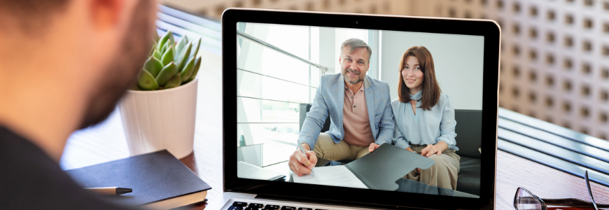 Couple signing a document virtually while a businessman watches them on screen