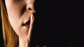 Serious woman placing her finger on lips representing one to keep quiet or keep a secret