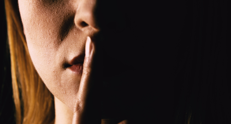 Serious woman placing her finger on lips representing one to keep quiet or keep a secret