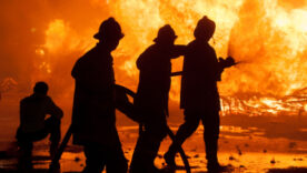 Silhouette of Firemen fighting a raging fire with huge flames of burning timber