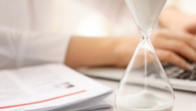 Hourglass and woman working on laptop at table in office