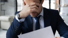 Unhappy businessman feeling stressed about bad news on a piece of paper.