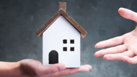 A hand is holding a model of a house and another set of hands is reaching for the house