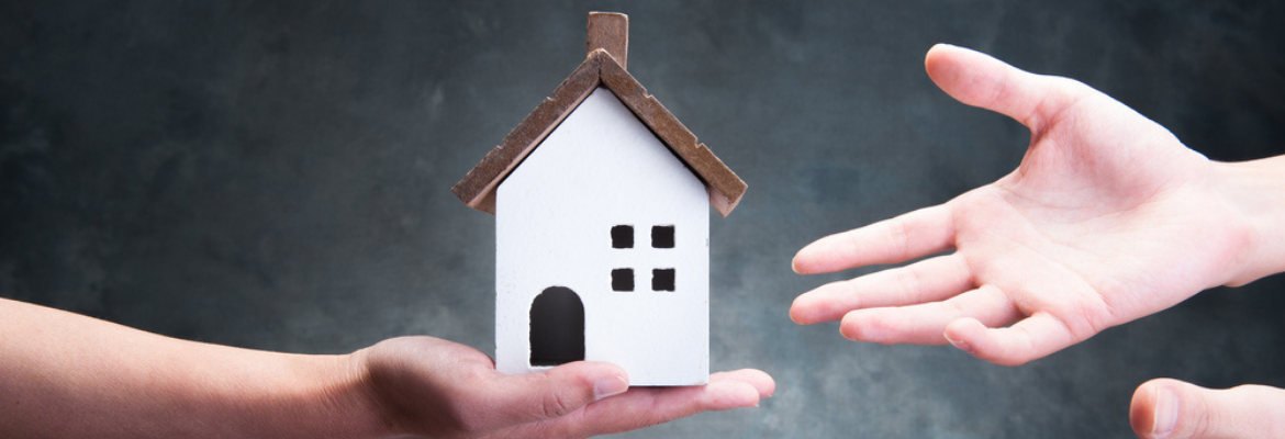 A hand is holding a model of a house and another set of hands is reaching for the house