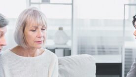 Mature couple sitting on couch, asking about document, signing papers with lawyer