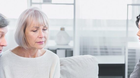 Mature couple sitting on couch, asking about document, signing papers with lawyer