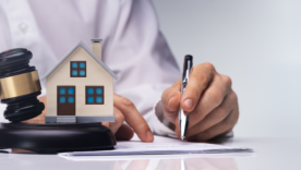Real Estate Lawyer in background with gravel and miniature house in front of him.