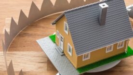 Mortgage house in a bear trap on wooden table background. House trap on debt or loan problem or risk in real estate property financing concept.