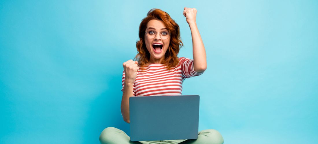 Woman sit with legs crossed work computer with her arms raised in fist pump