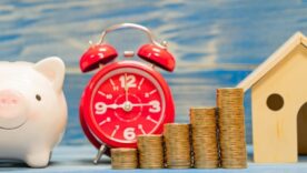 Piggy bank and stack gold coin with growing interest and home model and alarm clock with time in the office, Loan or saving money for buy house and asset and business investment in the future concept.