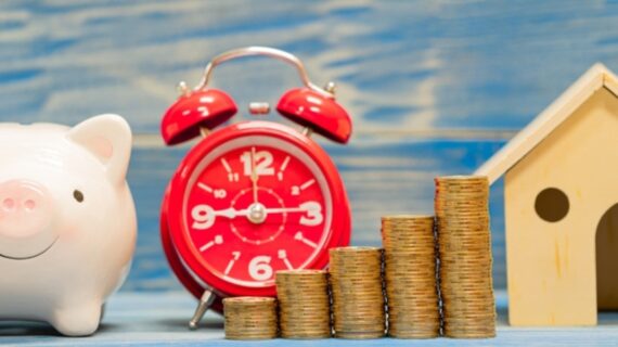 Piggy bank and stack gold coin with growing interest and home model and alarm clock with time in the office, Loan or saving money for buy house and asset and business investment in the future concept.