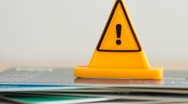 Close up yellow triangle emergency warning sign placed on a stack of credit cards