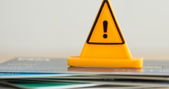 Close up yellow triangle emergency warning sign placed on a stack of credit cards