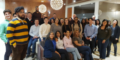 Pallett Valo staff members pose for a photo in a warmly lit indoor setting, seated and standing in a relaxed arrangement.