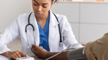 A healthcare professional in a white coat checks a patient's blood pressure in a modern clinic setting.