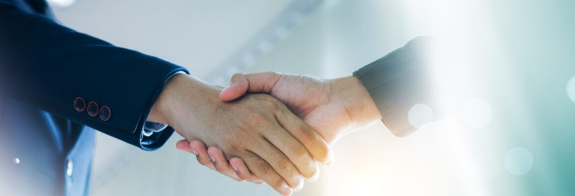 Two hands shaking in a professional setting, symbolizing agreement and collaboration between individuals in business attire.