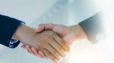 Two hands shaking in a professional setting, symbolizing agreement and collaboration between individuals in business attire.