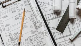 Architect design blueprints laid out on a desk with a pencil, ruler and other stationery items