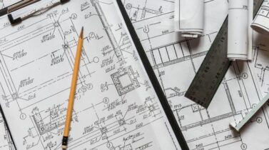 Architect design blueprints laid out on a desk with a pencil, ruler and other stationery items