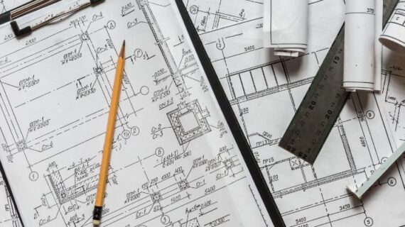 Architect design blueprints laid out on a desk with a pencil, ruler and other stationery items