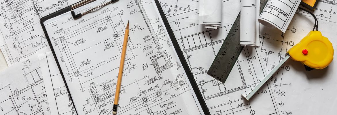 Architect design blueprints laid out on a desk with a pencil, ruler and other stationery items