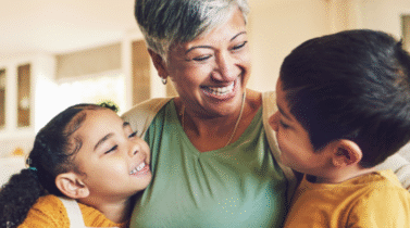 A grandmother and her two grandchildren sitting together and smiling on a couch