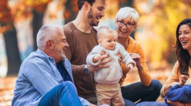 A family enjoys a picnic in an autumn park, surrounded by colorful leaves, while holding small children and sharing smiles.
