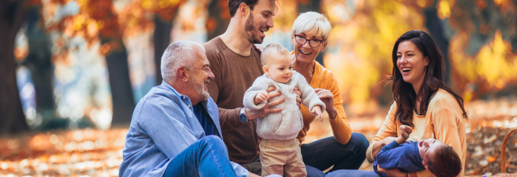 A family enjoys a picnic in an autumn park, surrounded by colorful leaves, while holding small children and sharing smiles.