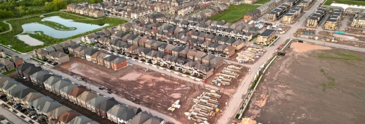 Aerial view of an Oakville suburban neighborhood featuring rows of homes, a small pond, and construction sites in a dirt area.