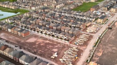 Aerial view of an Oakville suburban neighborhood featuring rows of homes, a small pond, and construction sites in a dirt area.