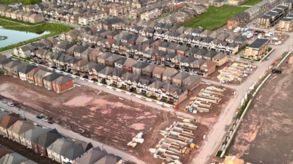 Aerial view of an Oakville suburban neighborhood featuring rows of homes, a small pond, and construction sites in a dirt area.