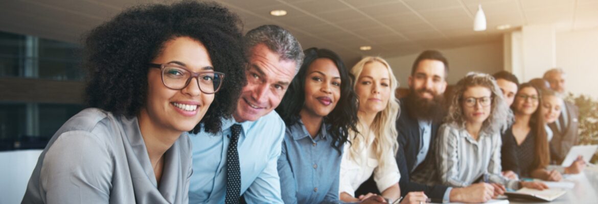 A diverse group of professionals sits in a modern conference room, focused intently during a meeting.