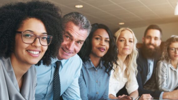 A diverse group of professionals sits in a modern conference room, focused intently during a meeting.