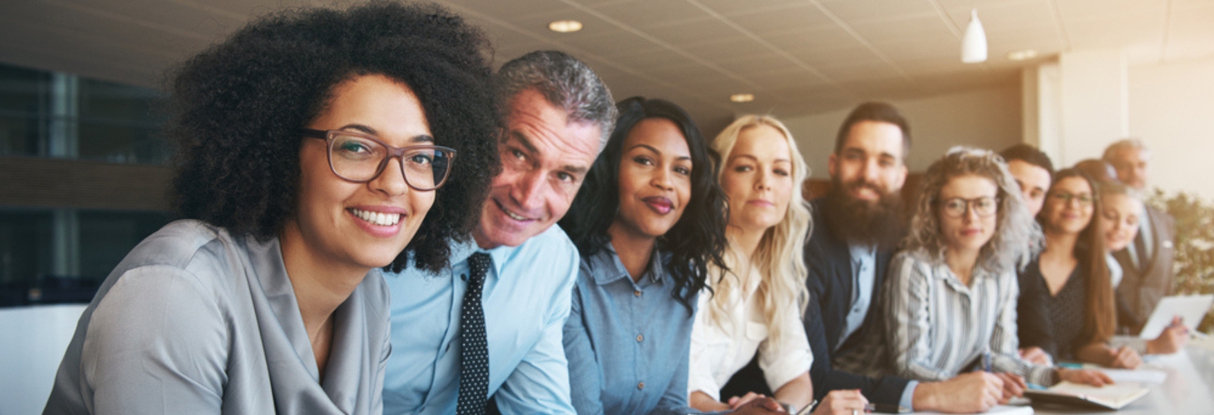 A diverse group of professionals sits in a modern conference room, focused intently during a meeting.