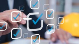 A business professional interacts with digital checkmarks while a yellow hard hat sits nearby, symbolizing project management or safety compliance.