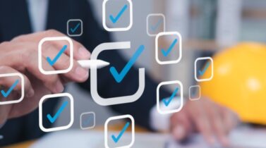 A business professional interacts with digital checkmarks while a yellow hard hat sits nearby, symbolizing project management or safety compliance.