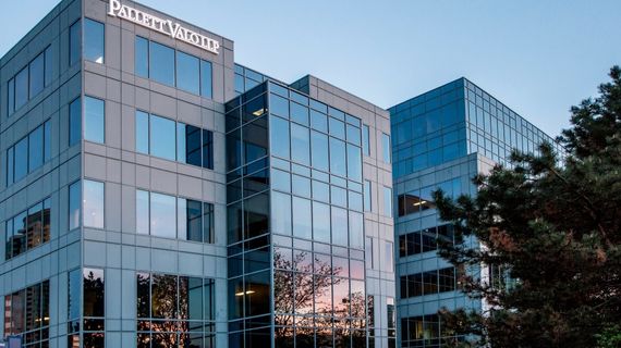 Pallett Valo office building with reflective glass windows, showing trees and evening sky, adjacent to tall pine trees.