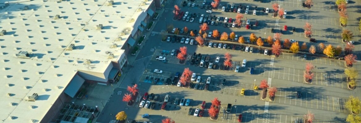 Aerial view of a parking lot with rows of cars and trees with autumn foliage near a large building.